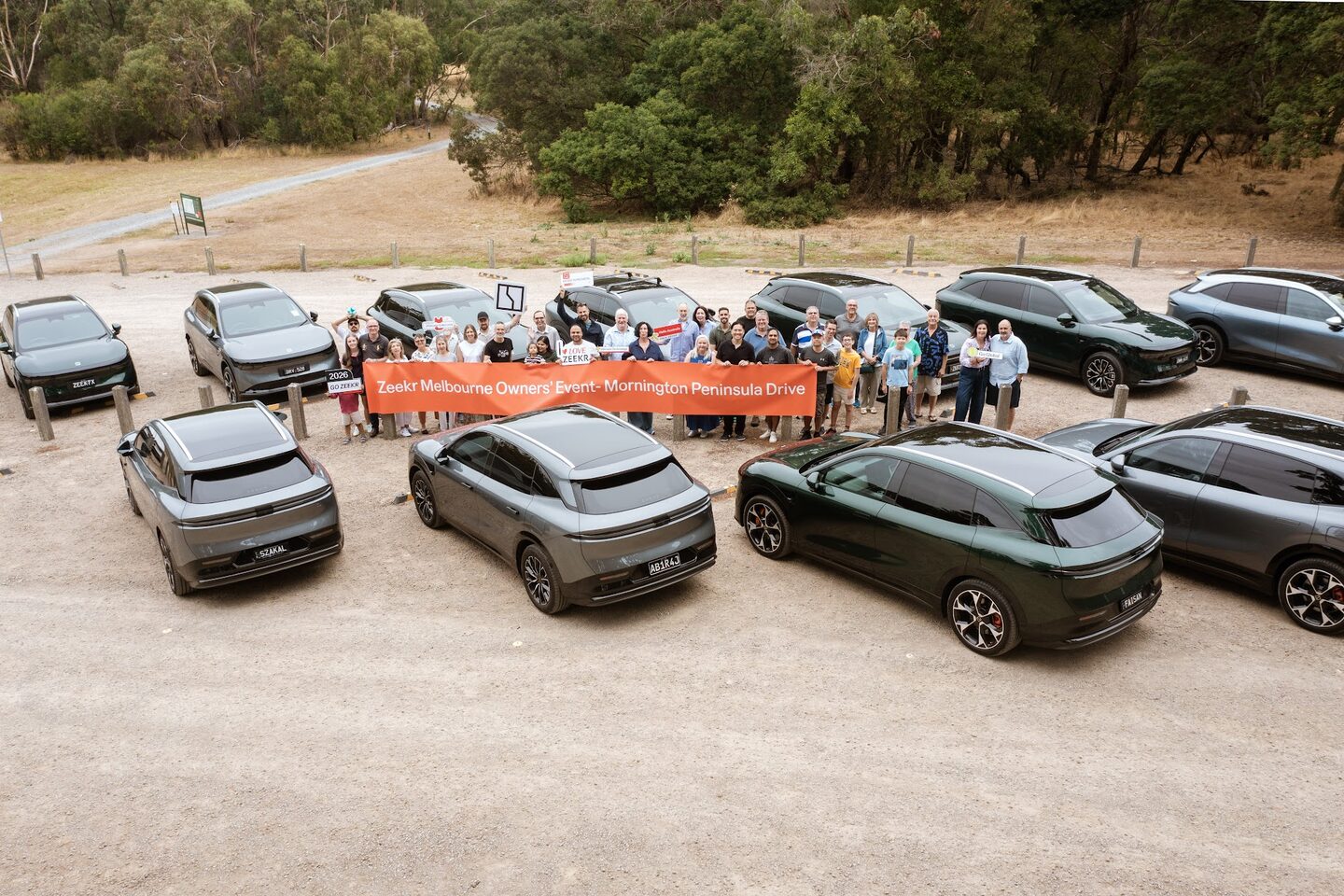 An aerial view of ZEEKR owners and families gathered around a Mornington Peninsula Drive banner, surrounded by parked ZEEKR vehicles.